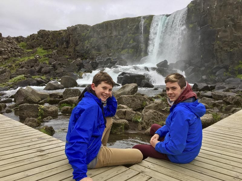 2 boys sitting in front of Öxarárfoss waterfall