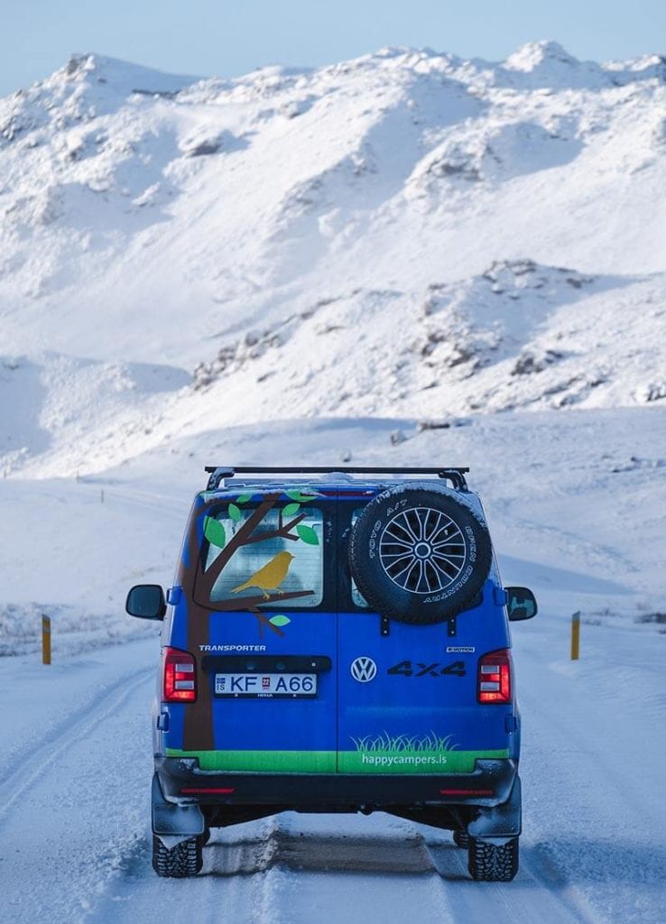 A blue 4x4 campervan on a snowy road with mountains in the background