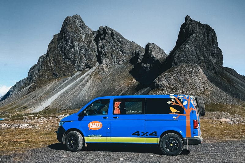 A blue campervan parked in front of a mountain