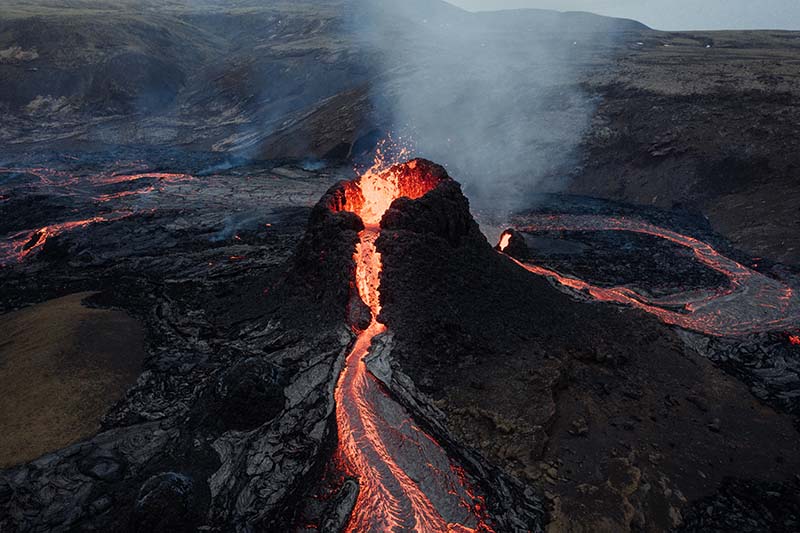 Volcano erruption in Iceland. Crater with orange streams of lava running downwards. 
