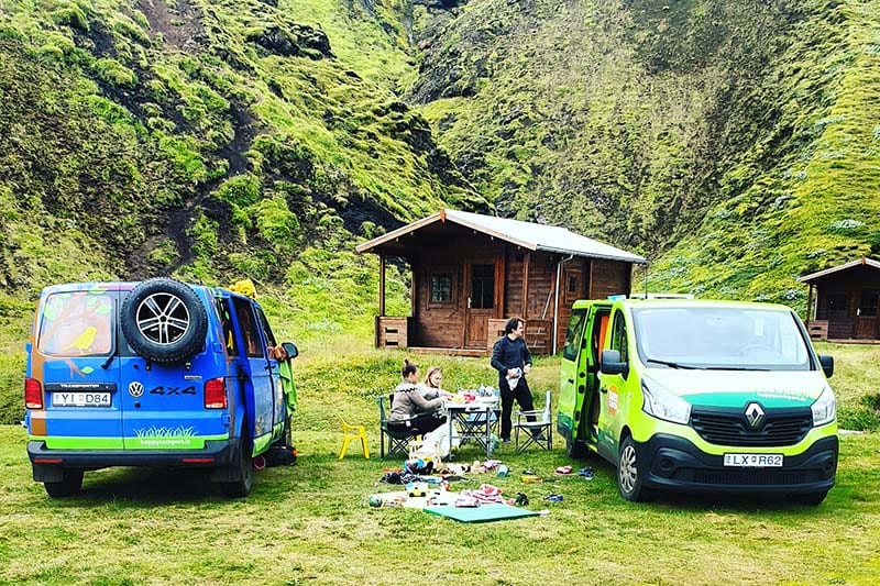 blue and green happy campervans parked in front of the a cabin with people camping