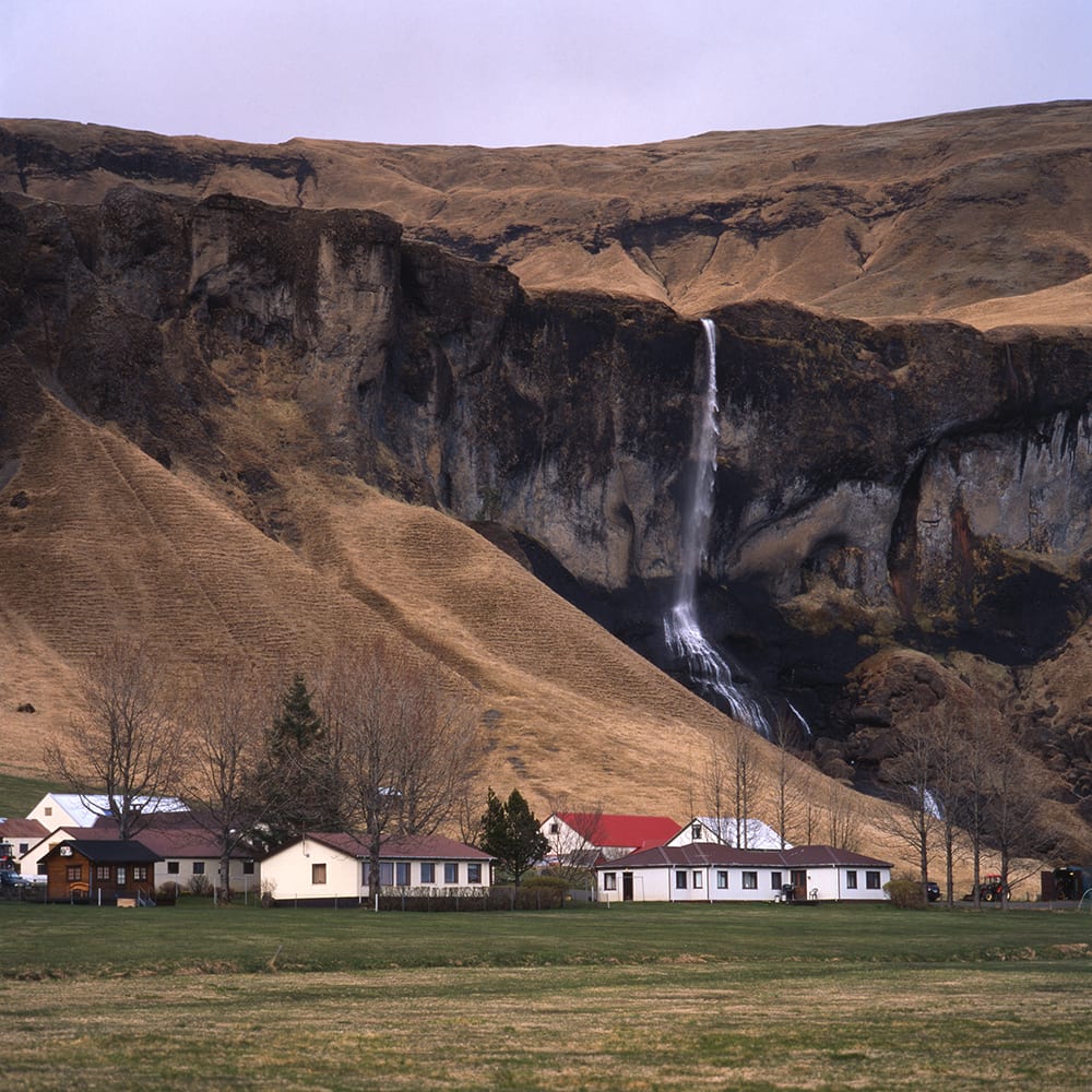 a cluster of small hauses at the foot of the mountain with a waterfall streaming down the mountain