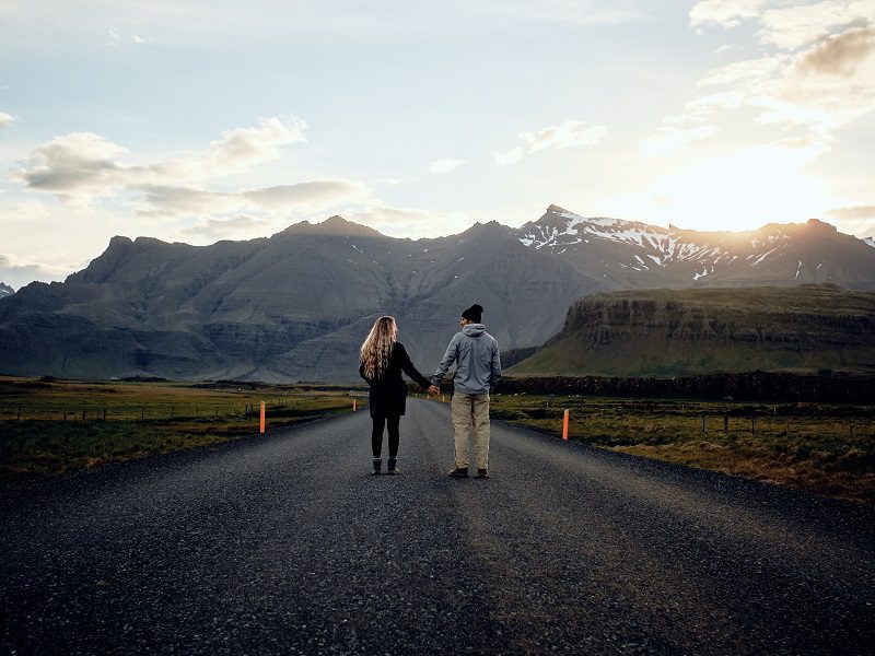 two people holding hands in the middle of an empty  road in iceland
