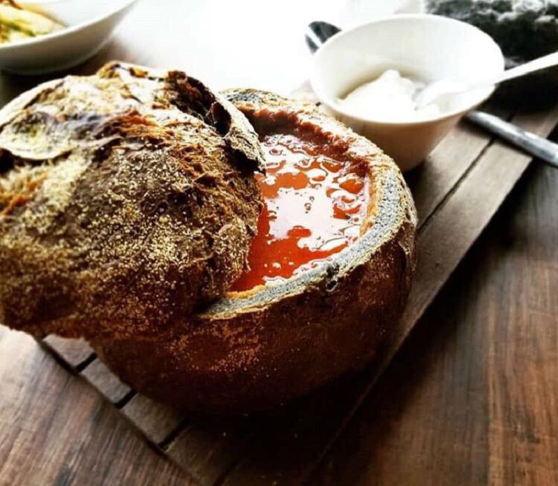 a bread bowl full of red soup on a wooden table
