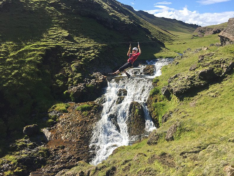 a man on a zipline above small waterfall 