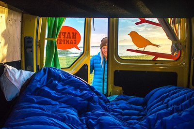 A girl opening happy camper door to see a bed made up with sleeping bags