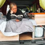 A woman relaxes with a book in the back of a campervan in Iceland