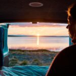 A person looks out from a van at a lake during sunset in Iceland, with the open door framing the view.