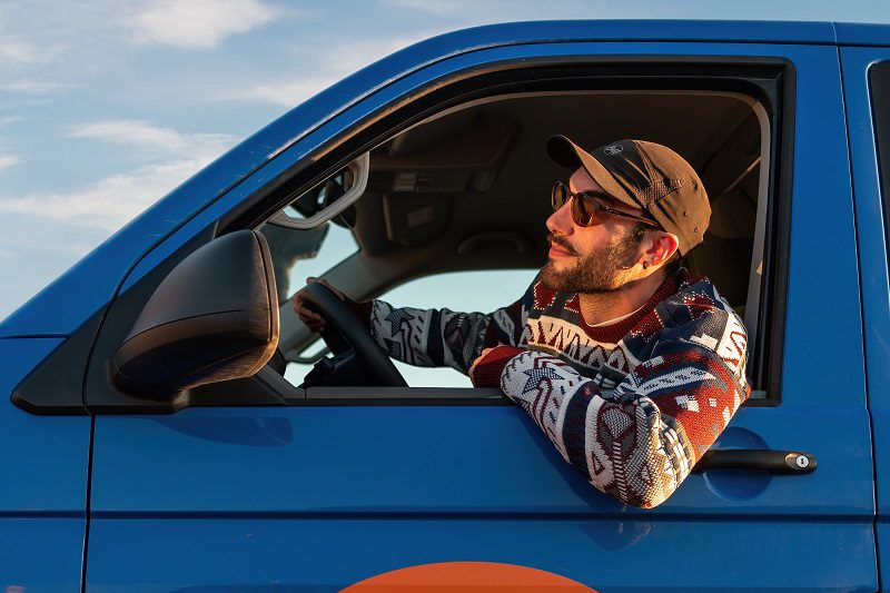 A man driving his Happy Camper campervan with his arm resting on the window