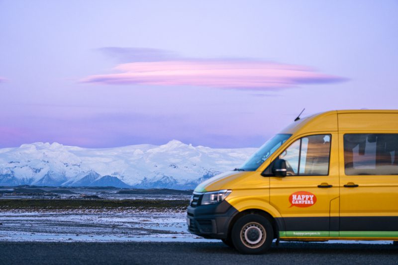 Yellow Happy Campers van parked in front of Icelandic glacier landscape during pastel-colored sunset