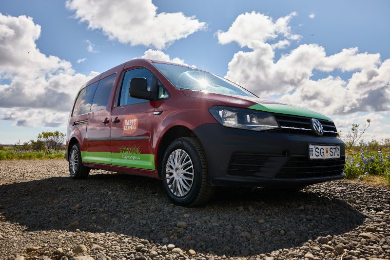 Front angle view of the Happy 1 EX AUTO campervan rental in Iceland, with a Volkswagen build, Happy Campers branding, and rugged tires for gravel roads.
