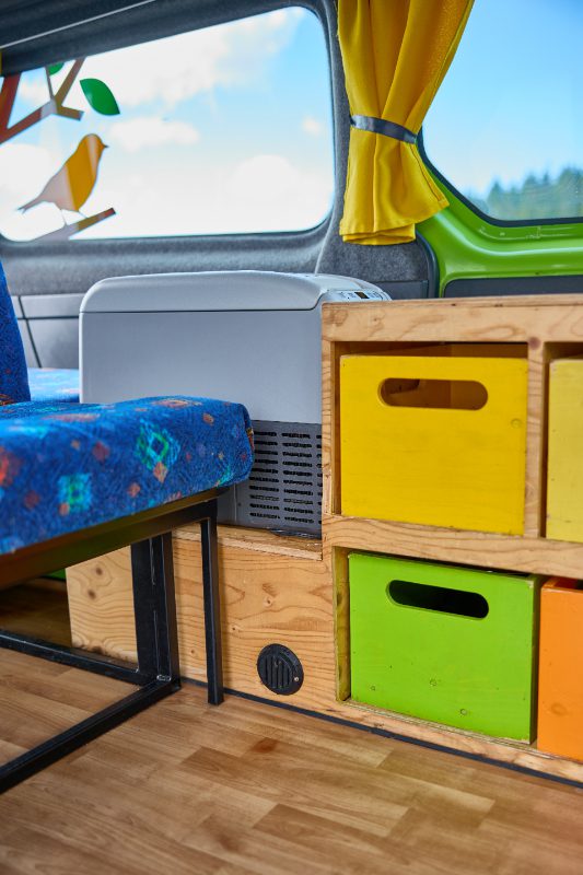 Close-up of the Happy 2 EX campervan’s interior featuring colorful storage drawers, built-in fridge, and wood-paneled kitchenette—compact and functional design for Icelandic road trips.