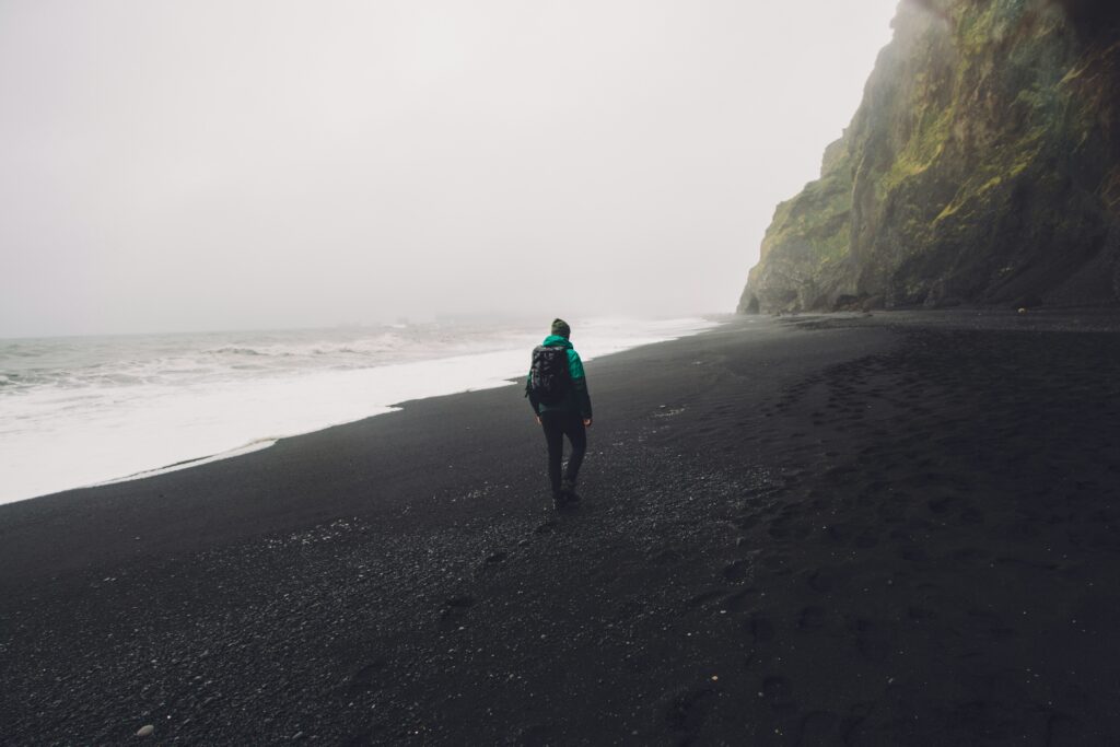 A man hiking along a black sand beach near Vík in Iceland